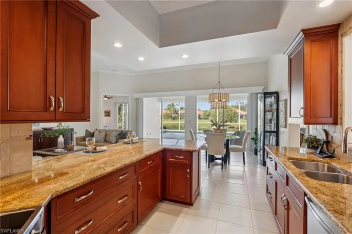 Kitchen featuring decorative backsplash, light stone counters, stainless steel dishwasher, sink, and decorative light fixtures