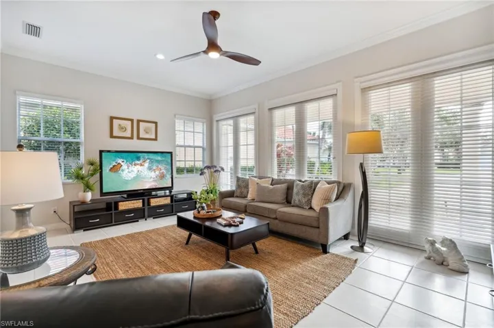 Living room with light tile patterned floors, ceiling fan, and crown molding