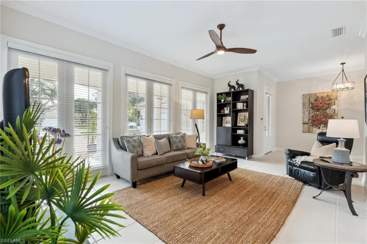 Living room featuring light tile patterned floors, ceiling fan with notable chandelier, a wealth of natural light, and ornamental molding