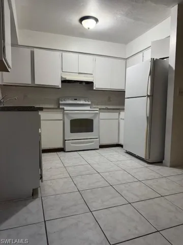 Kitchen with white cabinets, refrigerator, white electric stove, extractor fan, and light tile patterned floors