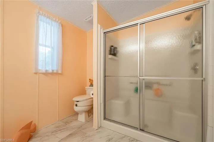 Bathroom with a textured ceiling, a stall shower, and marble look tile flooring