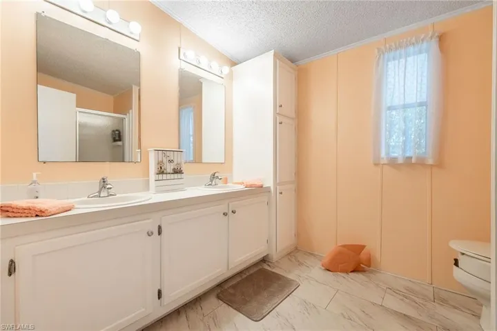 Full bathroom featuring a textured ceiling, a stall shower, double vanity, crown molding, and light marble finish flooring