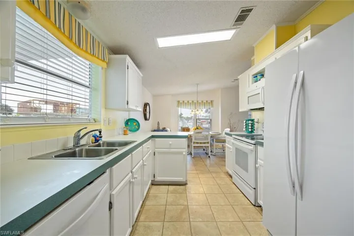 Kitchen with white appliances, white cabinets, a textured ceiling, decorative light fixtures, and vaulted ceiling