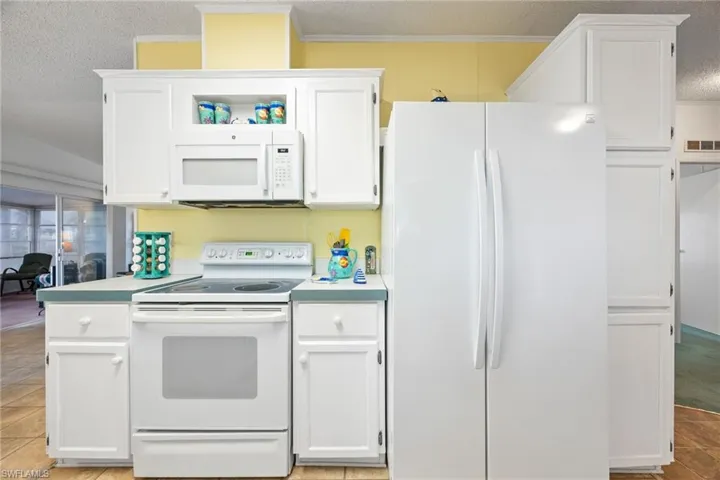 Kitchen with white appliances, white cabinetry, light countertops, and light tile patterned flooring