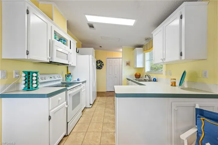Kitchen featuring white appliances, white cabinets, light tile patterned floors, light countertops, and a peninsula