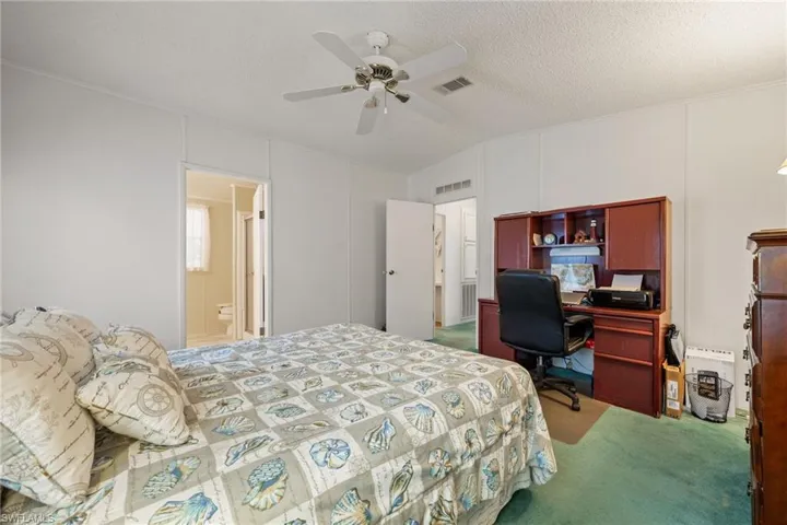 Master bedroom with light carpet, ceiling fan, a textured ceiling, lofted ceiling, and a decorative wall