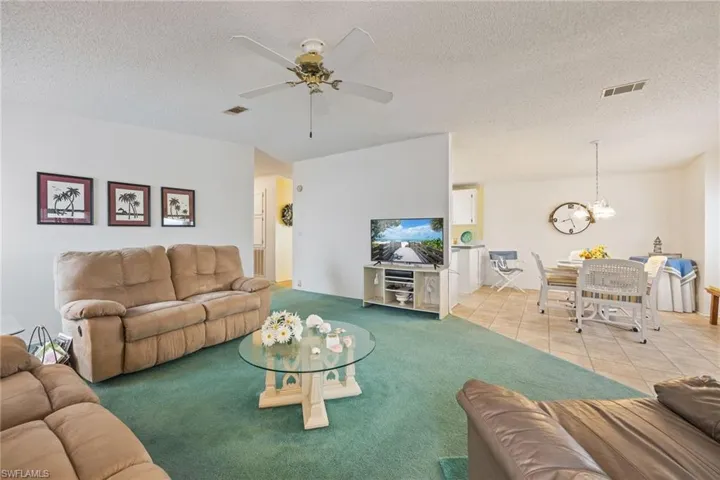 Living area with a textured ceiling, light tile patterned floors, a ceiling fan, and light colored carpet