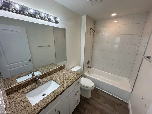 Bathroom with bathing tub / shower combination, vanity, and dark wood-type flooring