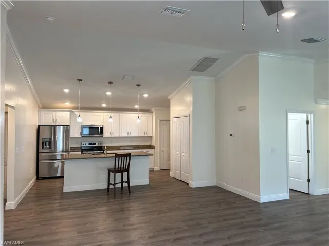 Kitchen featuring ornamental molding, stainless steel appliances, white cabinetry, dark wood finished floors, and a center island with sink