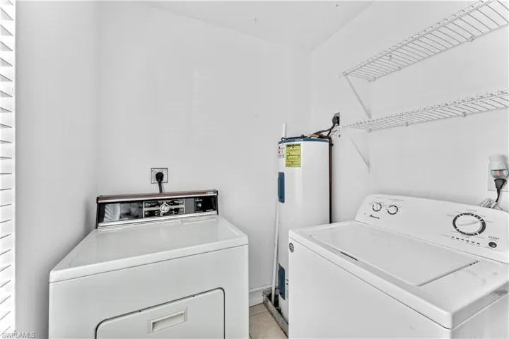 Clothes washing area featuring electric water heater, light tile patterned floors, and washer and dryer
