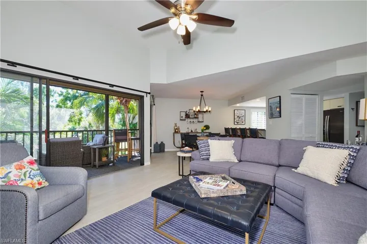 Living area featuring ceiling fan with notable chandelier, a towering ceiling, and wood finished look LTV floors