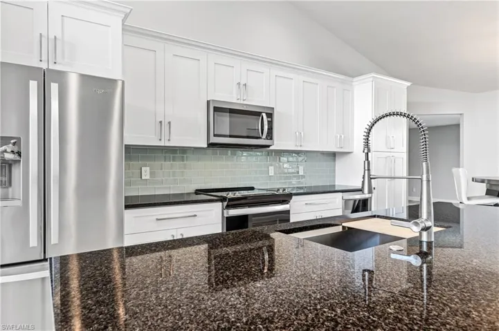 Kitchen with lofted ceiling, dark stone countertops, stainless steel appliances, backsplash, and white cabinetry