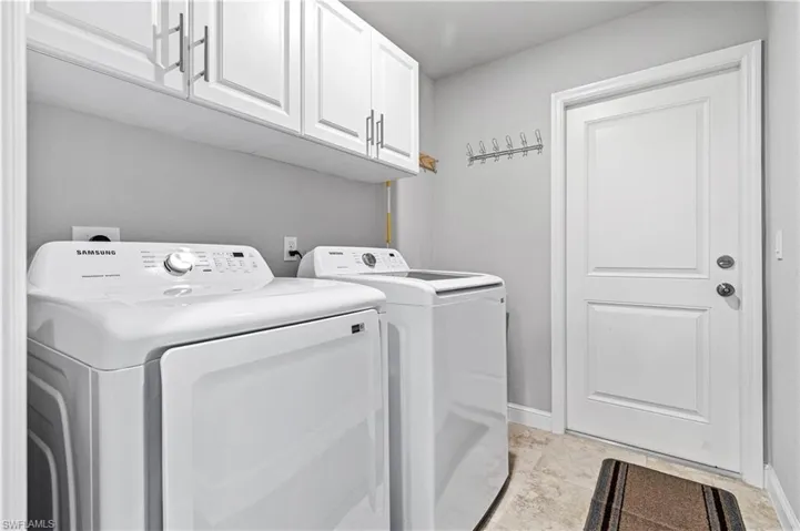 Washroom featuring cabinet space, washer and clothes dryer, and light stone finish floors
