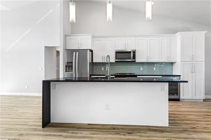 Kitchen with white cabinetry, high vaulted ceiling, stainless steel appliances, decorative backsplash, and dark stone counters