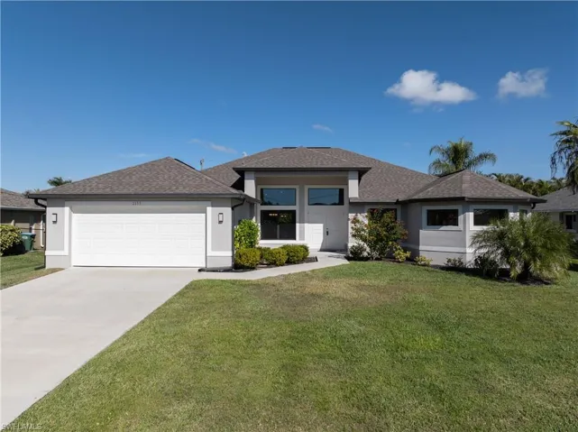 Prairie-style home featuring a shingled roof, a front lawn, driveway, and stucco siding