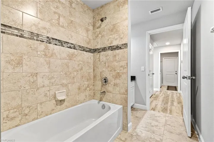 Bathroom featuring washtub / shower combination, light tile patterned flooring, and vanity