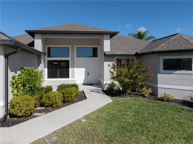 View of exterior entry featuring a shingled roof, stucco siding, and a yard
