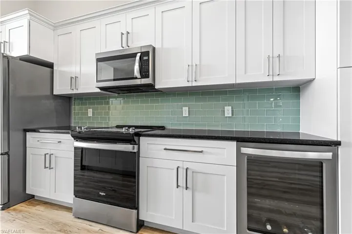 Kitchen with beverage cooler, appliances with stainless steel finishes, dark stone countertops, and white cabinetry