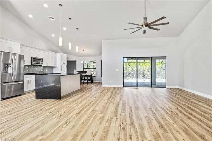 Kitchen with high vaulted ceiling, open floor plan, appliances with stainless steel finishes, white cabinets, and a kitchen island with sink