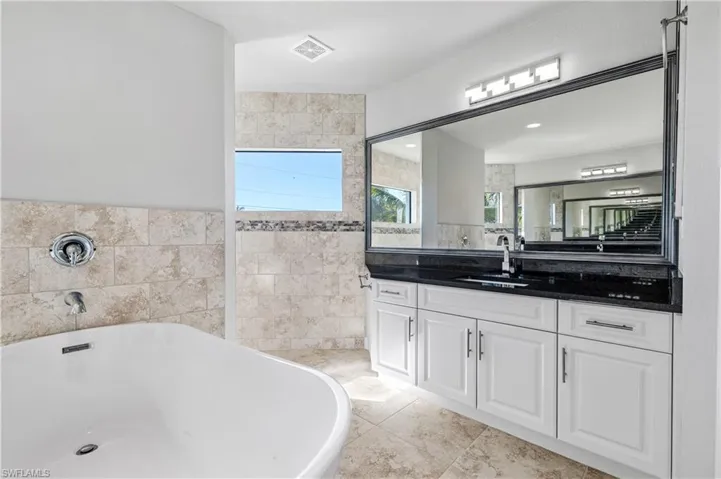 Bathroom with a freestanding tub, vanity, tile walls, and light tile patterned floors