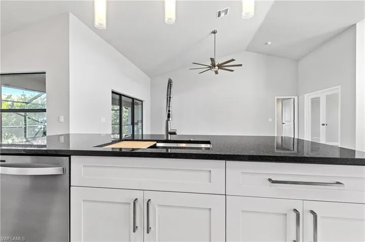 Kitchen with stainless steel dishwasher, dark stone countertops, white cabinetry, high vaulted ceiling, and open floor plan