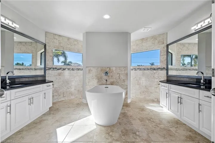 Bathroom with a soaking tub, two vanities, plenty of natural light, tile walls, and recessed lighting