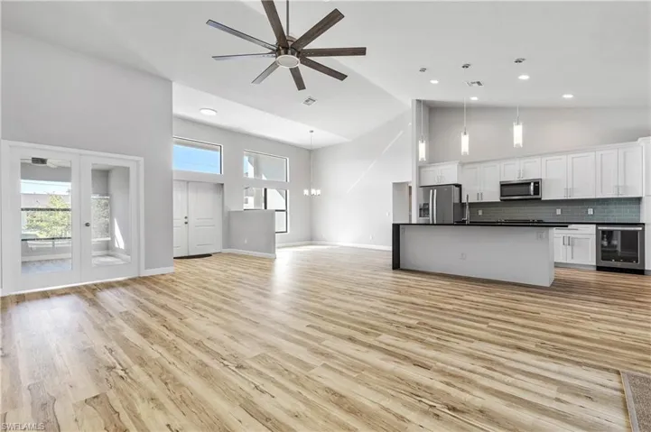Unfurnished living room featuring a ceiling fan, high vaulted ceiling, wine cooler, a chandelier, and light wood-style flooring