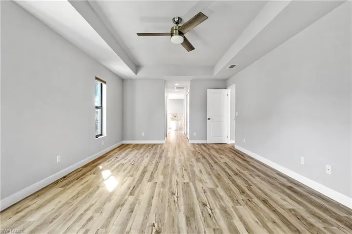 Unfurnished bedroom with a raised ceiling, light wood-type flooring, a ceiling fan, and connected bathroom