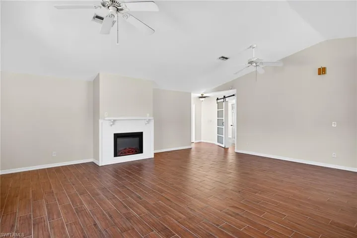 Unfurnished living room featuring a barn door, a ceiling fan, vaulted ceiling, wood tiled floors, and a glass covered fireplace