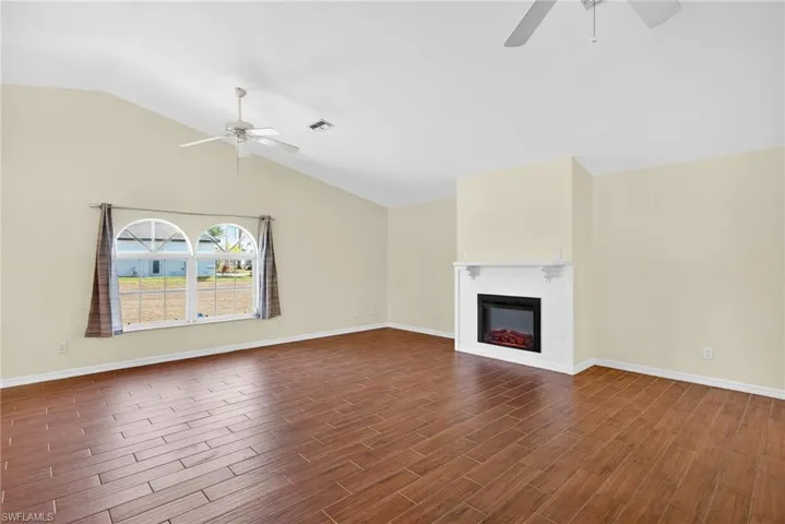 Unfurnished living room with a ceiling fan, wood finish floors, lofted ceiling, and a glass covered fireplace