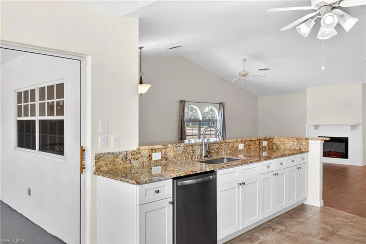 Kitchen featuring a peninsula, light stone countertops, white cabinets, a fireplace, and open floor plan