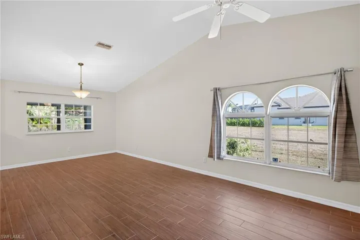 Empty room with lofted ceiling, wood tiled floors, healthy amount of natural light, and ceiling fan