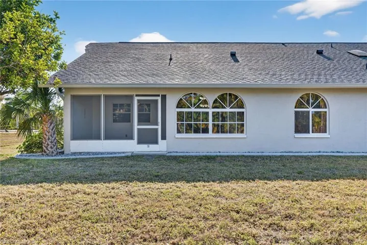 Back of property with stucco siding, a sunroom, roof with shingles, and a lawn