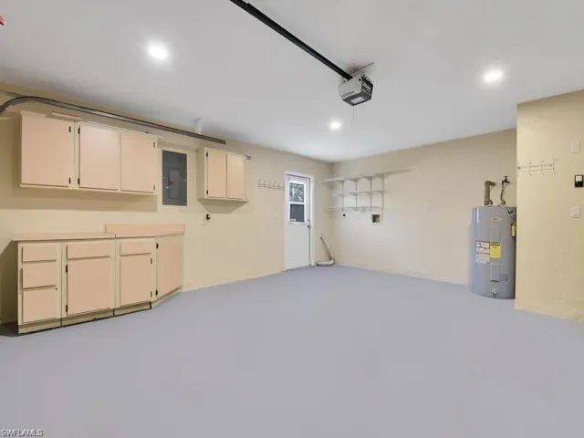 Garage with electric water heater, electric panel, recessed lighting, and a garage door opener