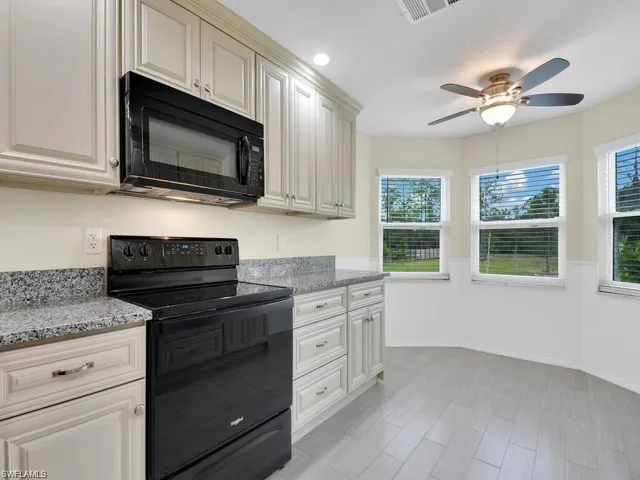 Kitchen featuring black appliances, wainscoting, light stone counters, a ceiling fan, and recessed lighting