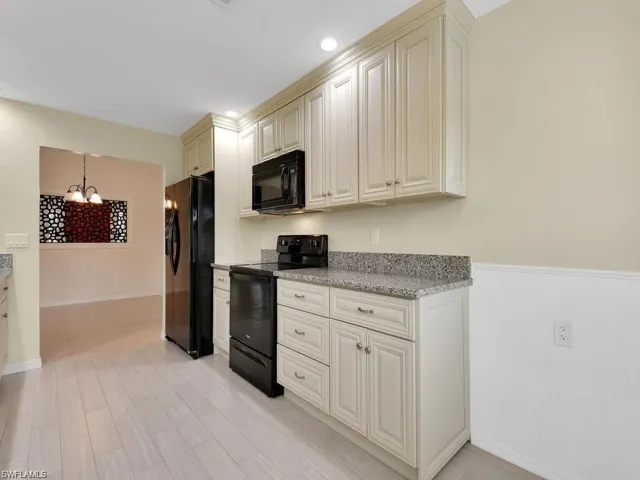 Kitchen featuring black appliances, light stone countertops, suspended lighting, cream cabinets, and a wainscoted wall
