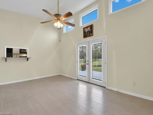 Unfurnished living room featuring french doors, a high ceiling, healthy amount of natural light, a ceiling fan, and light wood-type flooring