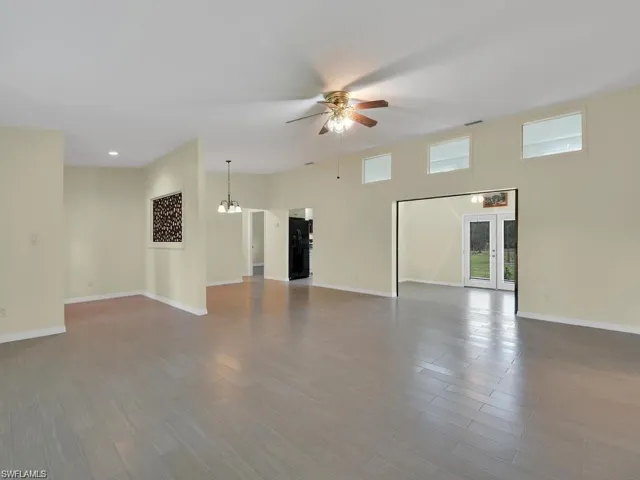 Unfurnished living room featuring french doors, ceiling fan, dark wood finished floors, and a chandelier