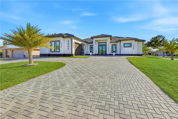 Prairie-style house featuring a front yard, decorative driveway, an attached garage, and stucco siding