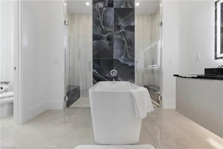 Full bathroom featuring a marble finish shower, a soaking tub, tile walls, light marble finish floors, and vanity