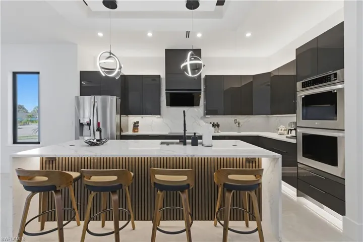 Kitchen with modern cabinets, a kitchen breakfast bar, light stone counters, an island with sink, and pendant lighting