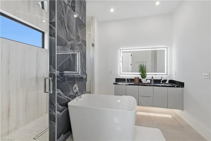 Bathroom featuring double vanity, a marble finish shower, a soaking tub, and recessed lighting