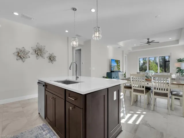 Kitchen featuring dark brown cabinetry, pendant lighting, light stone countertops, open floor plan, and a ceiling fan