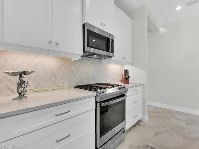 Kitchen featuring stainless steel appliances, tasteful backsplash, white cabinets, light stone counters, and light marble finish flooring