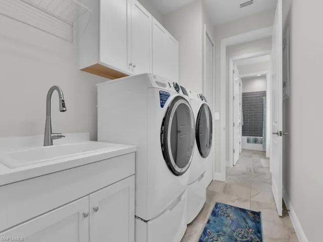 Washroom featuring washer and clothes dryer, cabinet space, and light marble finish floors