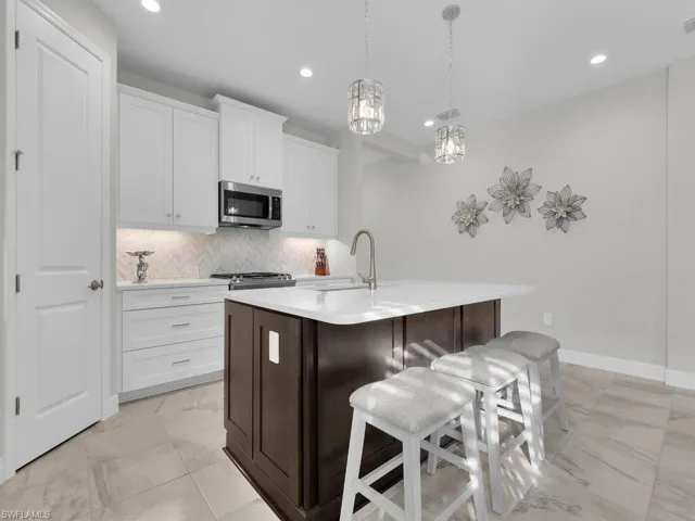 Kitchen featuring white cabinetry, tasteful backsplash, a kitchen bar, appliances with stainless steel finishes, and dark brown cabinets