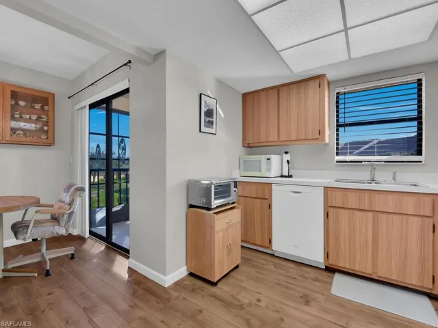 Kitchen with light brown cabinetry, light countertops, white appliances, and light wood-style floors