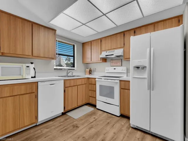 Kitchen with white appliances, light countertops, under cabinet range hood, light wood finished floors, and light brown cabinets