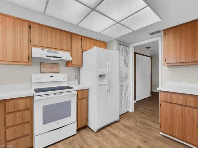Kitchen with white appliances, light countertops, under cabinet range hood, light wood-type flooring, and a paneled ceiling