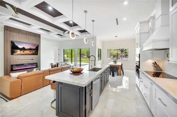 Kitchen featuring white cabinets, light stone countertops, coffered ceiling, open floor plan, and pendant lighting